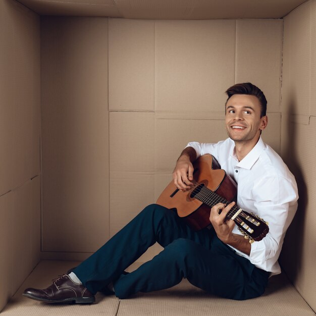 Junger Mann im Hemd, das Gitarre in der Pappschachtel spielt.