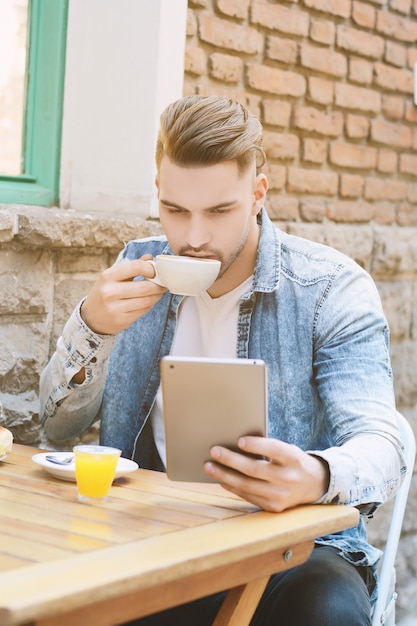 Junger Mann im Kaffeestubekaffee unter Verwendung einer Tablette.