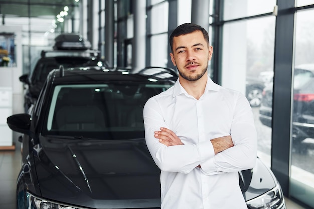 Junger Mann im weißen Hemd ist drinnen mit modernen neuen Automobilen