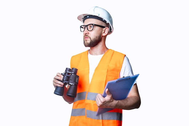 Junger Mann in Baukleidung, mit Fernglas, mit einem Klemmbrett auf hellem Hintergrund.