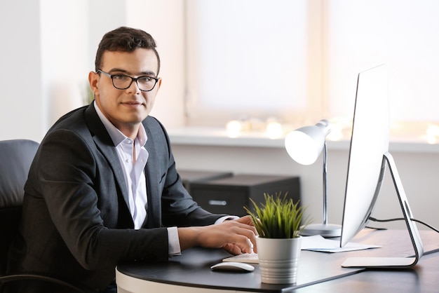 Junger Mann in Bürokleidung, der am Tisch mit Computer arbeitet