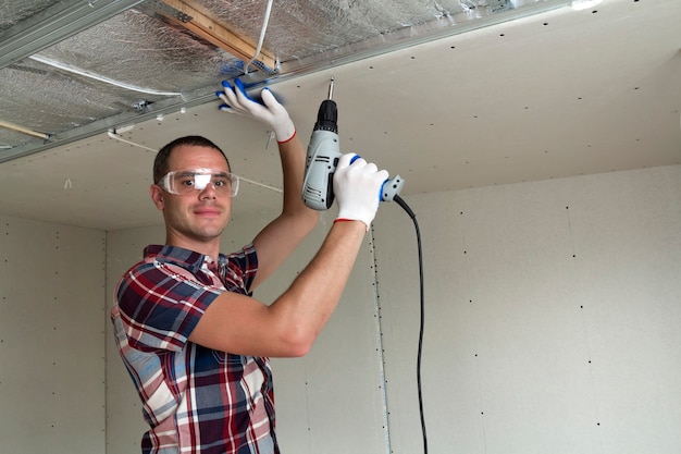 Junger Mann in der Schutzbrille, die Trockenbau-abgehängte Decke an Metallrahmen befestigt