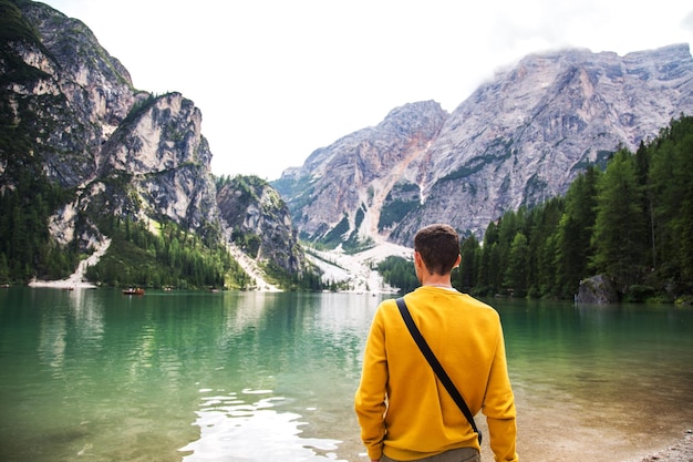 Junger Mann in einem gelben Sweatshirt, der vor dem Lago di Braies in den Dolomiten Italien steht