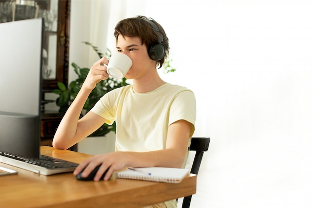 junger Mann in einem gelben T-Shirt arbeitet zu Hause am Computer. Online chatten. Remote-Arbeit über das Internet bei Isolation während der Quarantäne des Coronavirus. Freiberufler