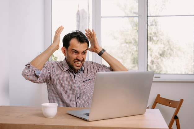 Junger Mann in einem Hemd, das an einem Laptop zu Hause arbeitet