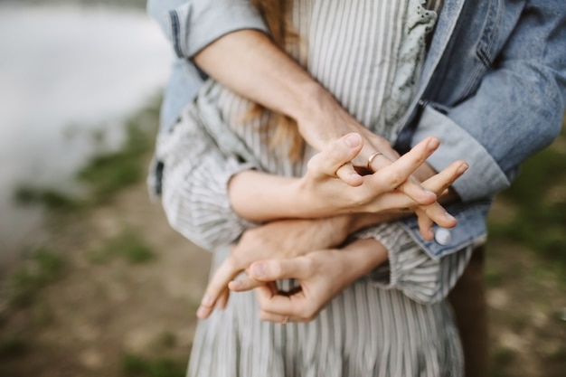 Junger Mann in einem Jeanshemd umarmt und hält die Hand einer schönen Frau. Nahaufnahmehände zusammen.