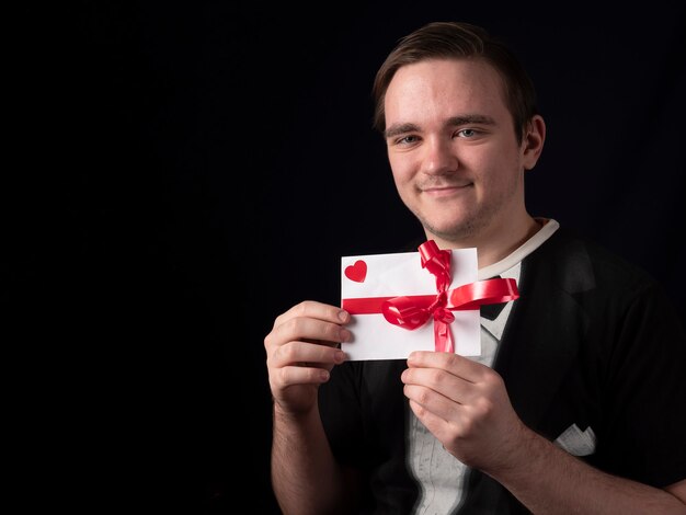 Junger Mann in einem schwarzen T-Shirt Anzug lächelnd und zeigt eine weiße Postkarte auf einem schwarzen Hintergrund