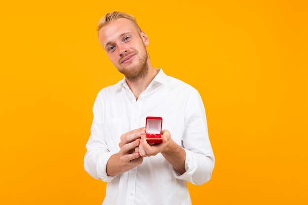 Junger Mann in einem weißen Hemd macht einen Heiratsantrag zu einem Mädchen, das einen Ring auf einem gelben Hintergrund hält