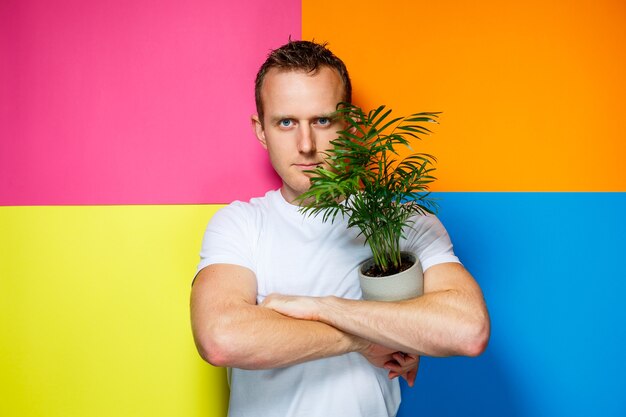 Junger Mann in einem weißen T-Shirt, bunter Hintergrund, dekorative Palme, Emotionsfoto, Heimpflanze, Liebe zur Natur