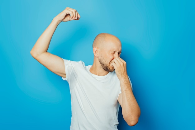 Junger Mann in einem weißen T-Shirt mit nassen Achselhöhlen vom Schweiß auf einem blauen Hintergrund