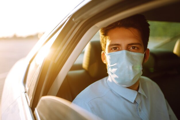 Junger Mann in einer Schutzmaske, die im Auto sitzt