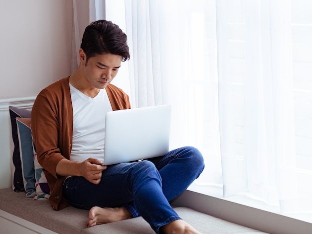 Junger Mann in Freizeitkleidung und mit Laptop