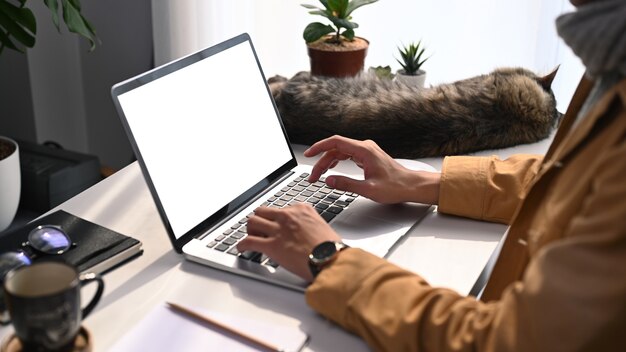 Junger Mann in gelber Jacke, der online mit Laptop-Computer im modernen Heimbüro arbeitet.