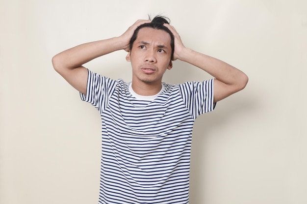Junger Mann in gestreiftem Hemd mit verwirrtem Gesichtsausdruck, während er sich auf isoliertem Hintergrund am Kopf kratzt