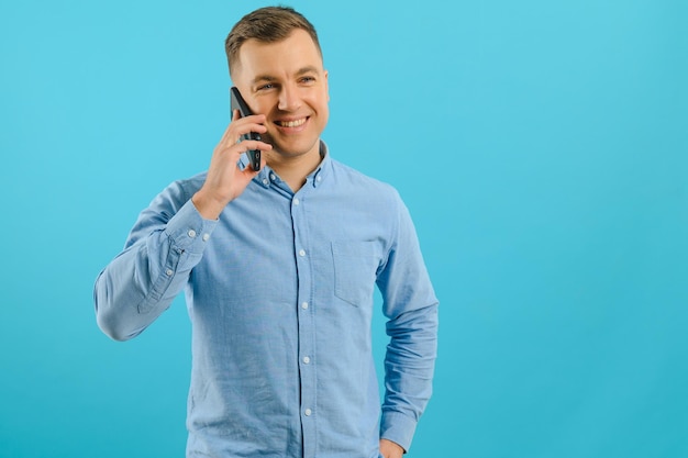 Junger Mann in heller, farbenfroher Kleidung, der auf einem Mobiltelefon auf blauem Hintergrund spricht Trendiger Typ hat ein Gespräch Smartphone-Technologiekonzept