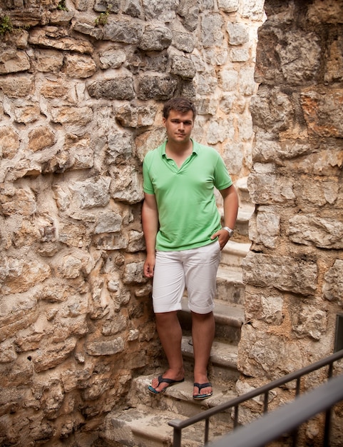 Junger Mann in Shorts, der sich an eine alte Steinmauer lehnt