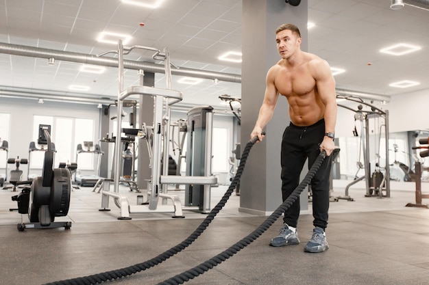 Junger Mann in Sportkleidung, der Übungen mit speziellem Seil im Fitnessstudio macht