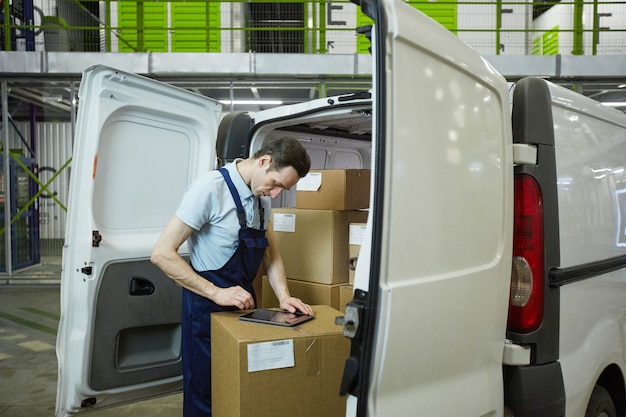 Junger Mann in Uniform registriert Paket mit digitalem Tablet vor der Lieferung