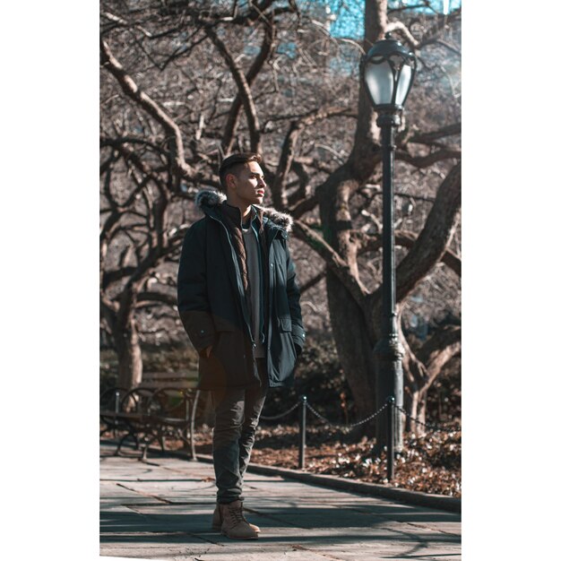 Foto junger mann in voller länge trägt einen pelzmantel, während er im park steht