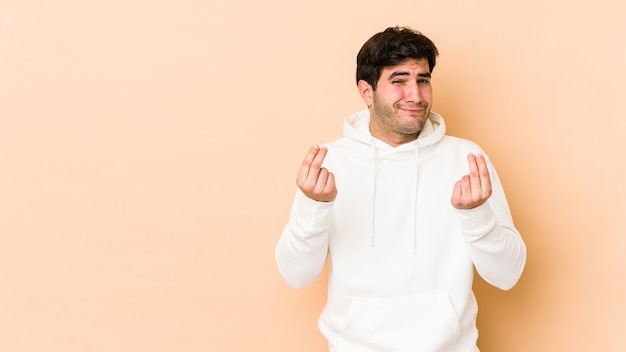 Junger Mann isoliert auf beige Wand zeigt, dass sie kein Geld hat.