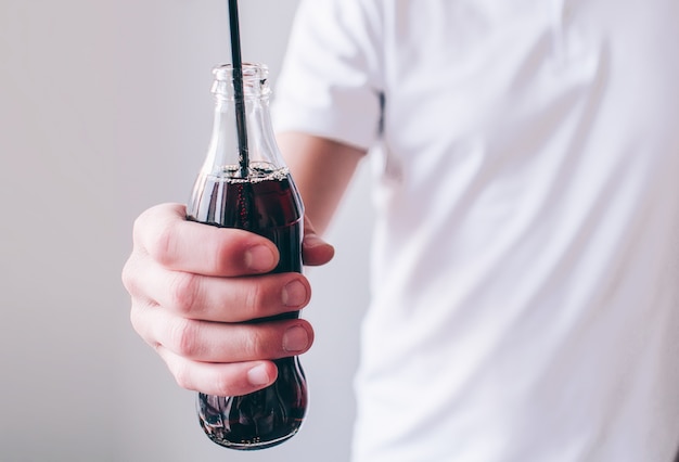 Junger Mann isoliert. Schnittansicht der Hand des Mannes, die Flasche mit Cola darin und schwarzem Plastikstroh hält. Süßes leckeres zuckerhaltiges Getränk.