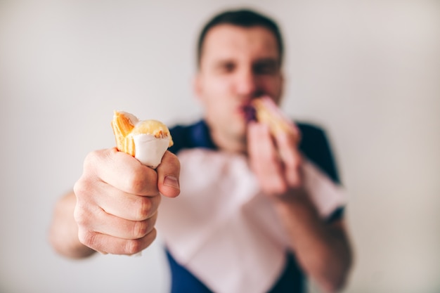 Junger Mann isoliert über defokussierte verschwommene Wand. Essen und verschlingen Sie leckere Mastkuchen.