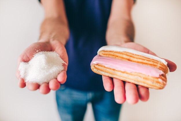 Junger Mann isoliert über Mauer. Konzentriertes Bild auf leckeren leckeren Kuchen in Händen. Prozess auswählen. Defokussierte verschwommene Wand.