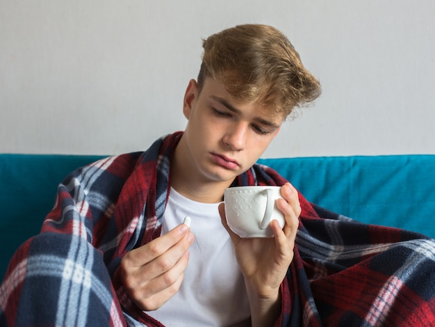 junger Mann ist grippekrank, liegt zu Hause unter einer Decke, nimmt eine Pille