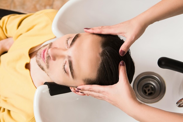 Junger Mann liegt mit geschlossenen Augen im Schönheitssalon. Schöner Mann, der sich im Friseursalon die Haare waschen lässt.