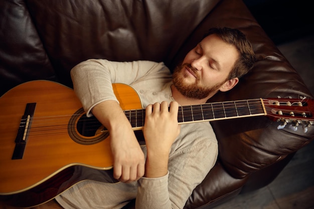 Junger Mann liegt mit Gitarre auf der Couch