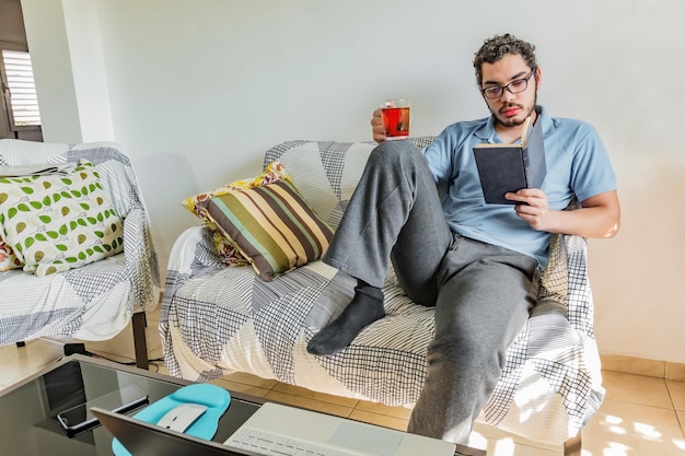 Junger Mann liest ein Buch und lernt, während er zu Hause auf der Couch sitzt