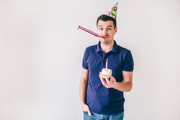 Junger Mann lokalisiert über weißem Hintergrund. Kerl halten kleinen Kuchen mit Kerze auf ihm, der Geburtstag feiert. Einsam auf Party. Allein feiern.