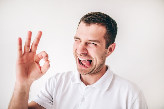 Junger Mann lokalisiert über weißer Wand. Emotionaler lustiger Kerl zeigt ok Symbol mit den Fingern.