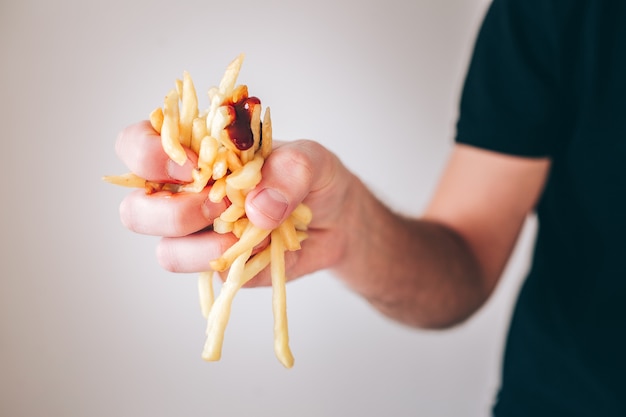 Junger Mann lokalisiert über weißer Wand. Schließen Sie herauf Bild der Hand, die Pommes Frites Kartoffel mit etwas Soße darüber hält. Ungesunde Fettmahlzeit.