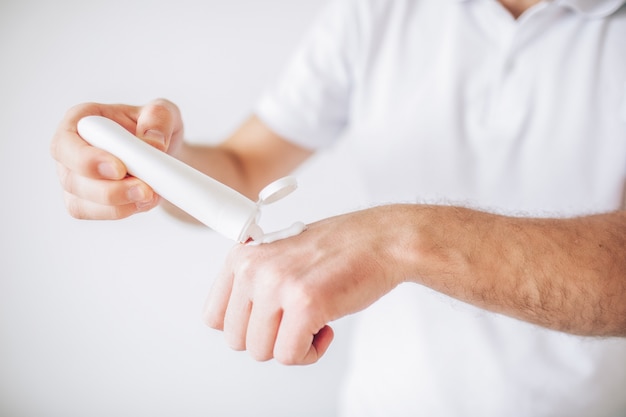 Junger Mann lokalisiert über weißer Wand. Schnittansicht der feuchtigkeitsspendenden Hände des Mannes. Creme zur Handpflege verwenden. Schönheitsbehandlungen und Behandlung.