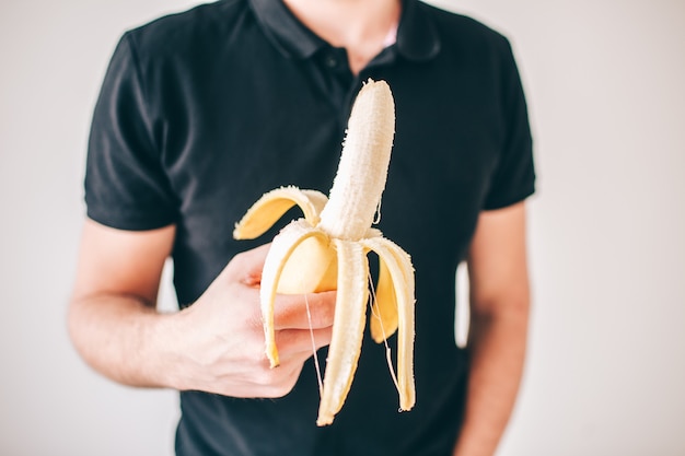 Junger Mann lokalisiert über weißer Wand. Schnittansicht und Nahaufnahme der geschälten gelben reifen Banane in den Händen des Mannes. Leckeres leckeres Obst.
