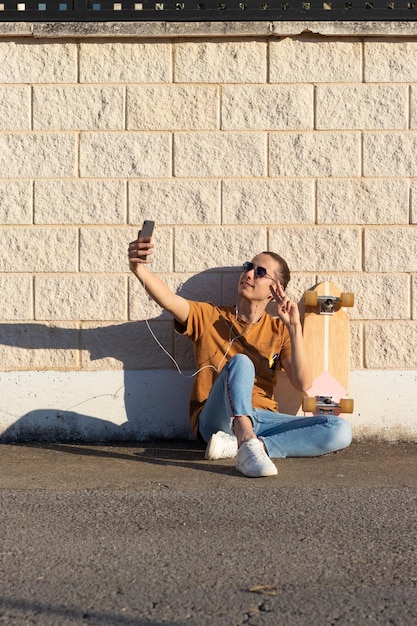 Junger Mann macht ein Selfie-Foto mit Stolz auf sein Skateboard, um es an Freunde zu senden, während er auf dem Boden sitzt