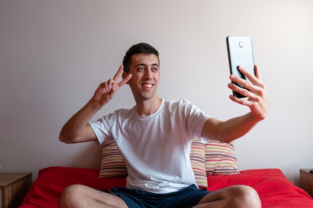 Junger Mann macht ein Selfie mit einem Tablet und macht mit seiner Hand das Friedenszeichen