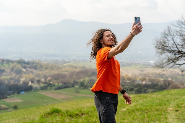 Junger Mann macht Selfie auf dem Handy auf dem Hügel