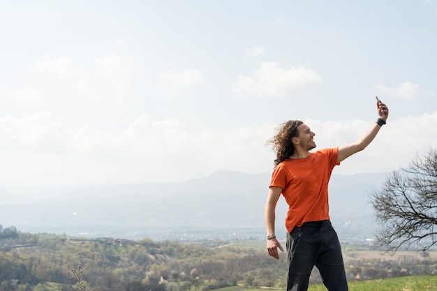 Junger Mann macht Selfie auf dem Handy auf dem Hügel