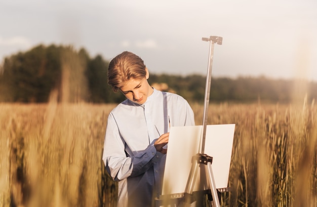 Junger Mann malt im Sommer auf Leinwand in der Natur. Künstlerische Arbeit in der Natur. Klare Luft.