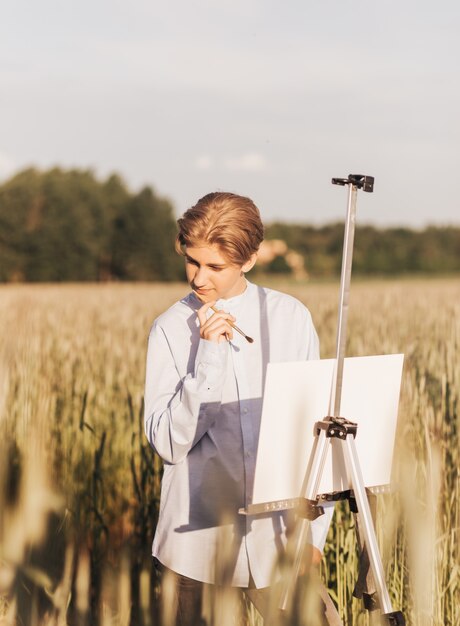 Junger Mann malt im Sommer auf Leinwand in der Natur. Künstlerische Arbeit in der Natur. Klare Luft.