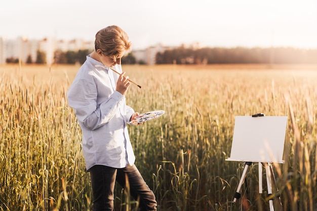 Junger Mann malt im Sommer auf Leinwand in der Natur. Künstlerische Arbeit in der Natur. Klare Luft.