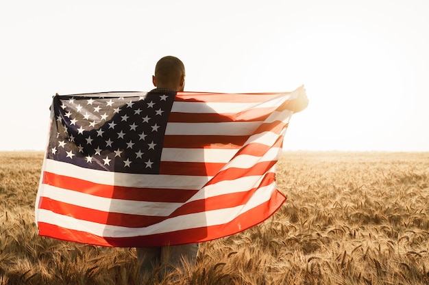 Junger Mann mit amerikanischer Flagge auf dem Rücken, während er im Weizenfeld steht