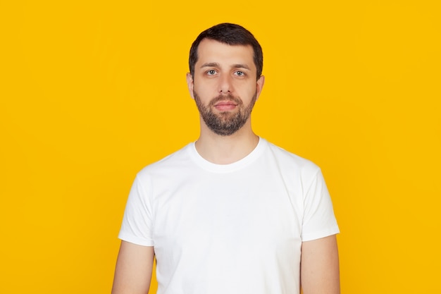 Junger Mann mit Bart in einem weißen T-Shirt mit einem ernsten Gesichtsausdruck.