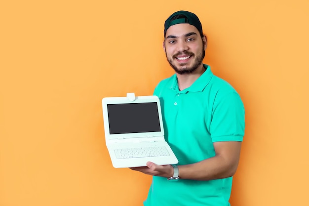 Junger Mann mit Bart, T-Shirt und grüner Kappe, der der Kamera ein Tablet mit Tastatur auf gelbem Hintergrund zeigt
