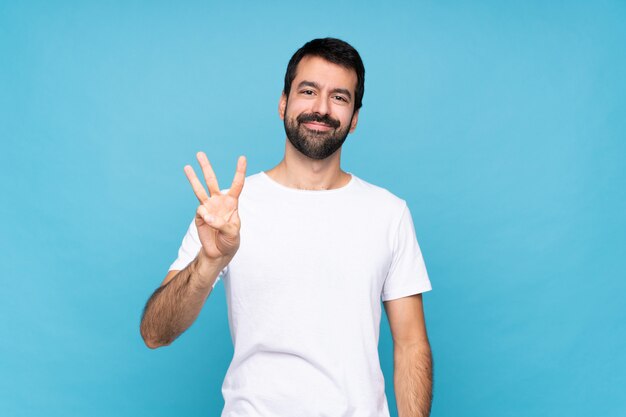 Junger Mann mit Bart über lokalisiertem blauem Hintergrund glücklich und drei mit den Fingern zählend