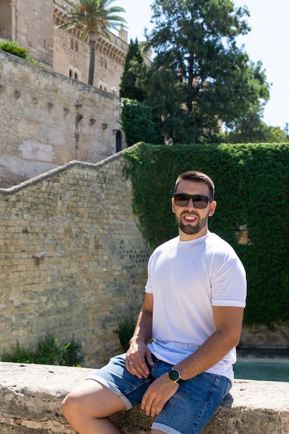 Junger Mann mit Bart und Sonnenbrille lehnt an einem sonnigen Tag in Spanien an der Wand in der Kathedrale von Palma de Mallorca