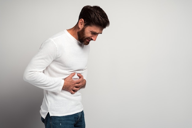 Junger Mann mit Bauchschmerzen. Junger Mann, der die Hände am Bauch hält, weil sich eine schmerzhafte Krankheit unwohl fühlt. Ache-Konzept