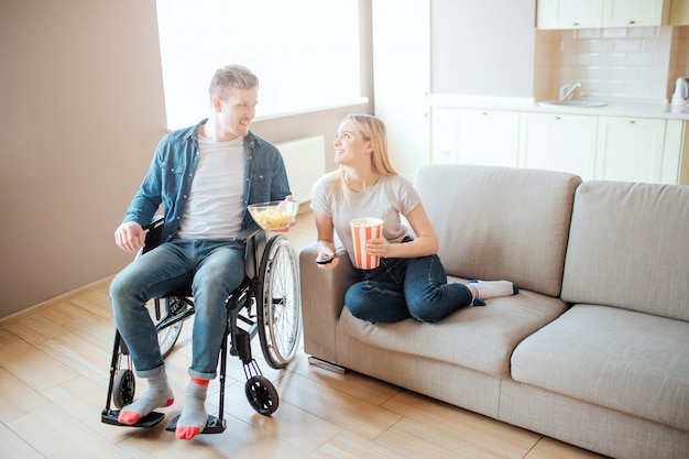 Junger Mann mit Behinderung sitzt neben Frau auf Sofa. Sie sehen sich an und sile. Film schauen. Heimkino. Liebe.